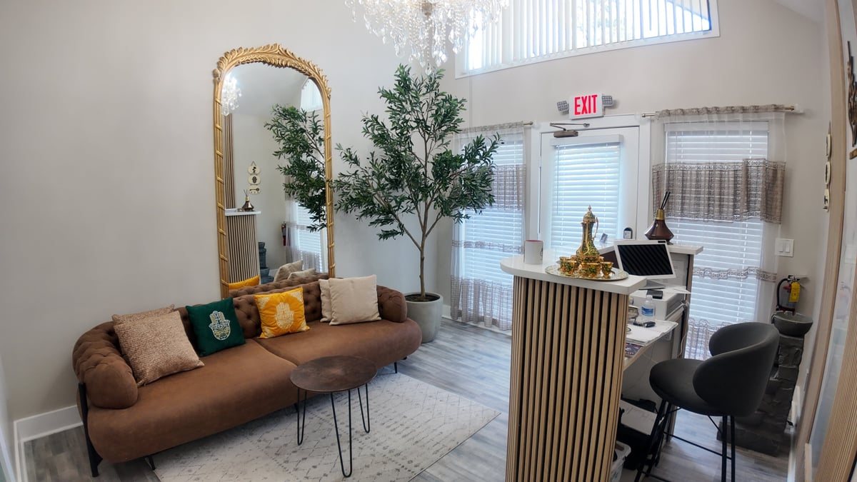 Modern office reception area with brown sofa, gold-framed mirror, potted tree, and front desk with checkout counter