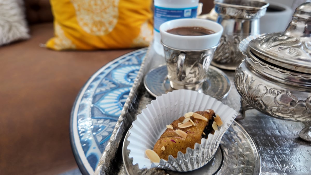 A chocolate pastry in a white wrapper on a blue and white patterned plate next to a cup of dark coffee and decorative items